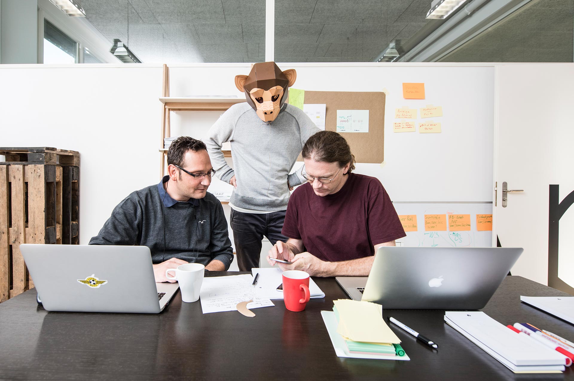 Olivier Oswald und Stephan Klaus an einem Tisch zusammen mit einer Person mit einer Affenmaske