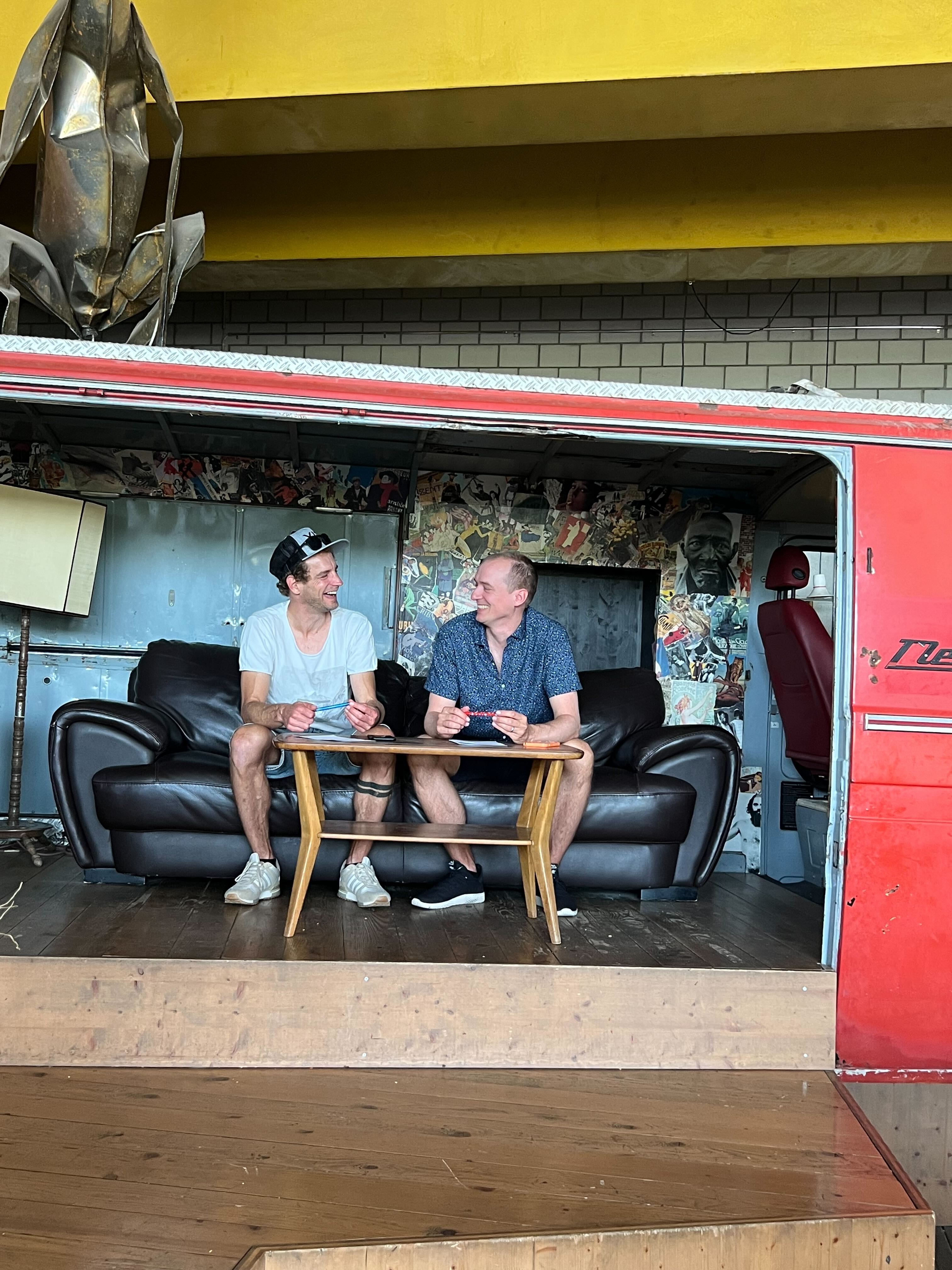 Roman Hofer und Raphael Neuenschwander sitzen nebeneinander auf einem Sofa und lachen sich an
