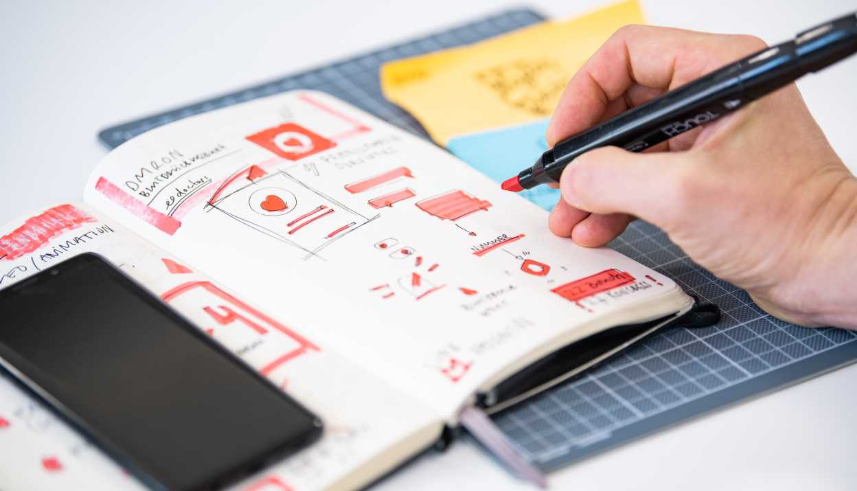 Notebook with sketches in which a hand draws something with a colored marker