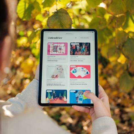 Le petit calendrier wird auf einem Tablet angeschaut, im Hintergrund sind Blätter eines Baumes