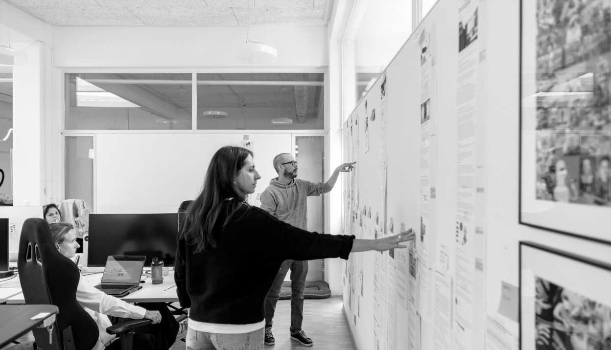 Das Marketing und Sales Team schaut gemeinsam Texte an, die an einer Wand im Büro aufgehängt sind.