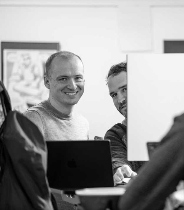 Raphael and Martin standing at a desk, laughing at the camera