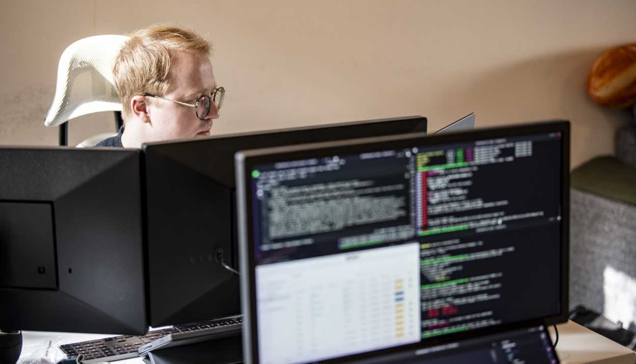 Web developer Kajetan Som is concentrating on his work behind a monitor displaying code