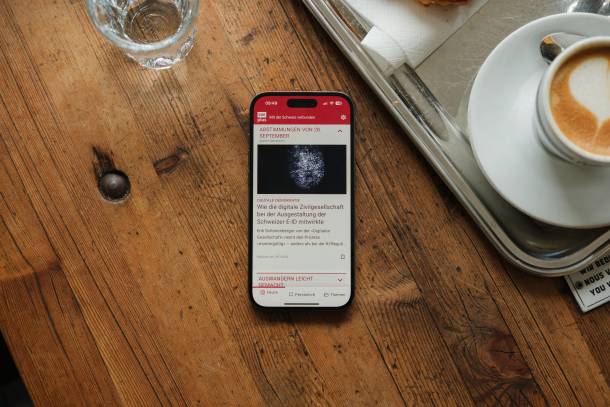 Samrtphone liegt auf einem Holztisch neben einer Tasse Kaffee und einem Wasserglas, geöffnet ist die SWIplus App