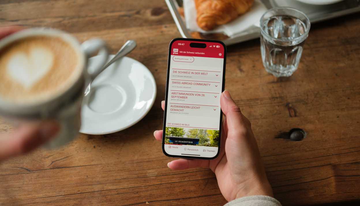SWIplus App geöffnet auf einem Smartphone in der Hand einer Person, die Kaffee trinkt