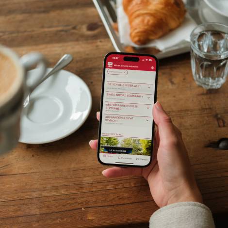 SWIplus App geöffnet auf einem Smartphone in der Hand einer Person, die Kaffee trinkt