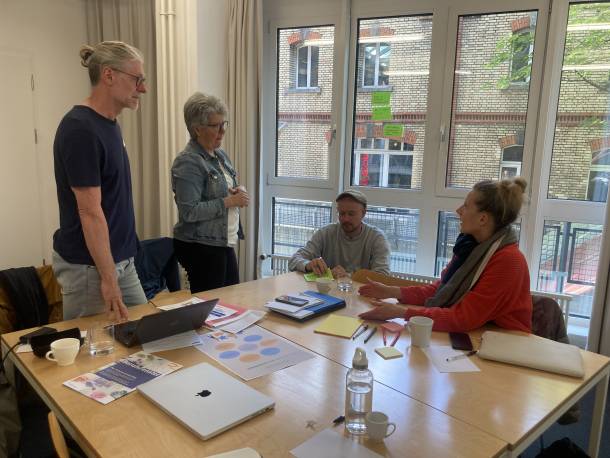 Personen stehen und sitzen rund um einen Tisch, sammeln auf Post-its Ideen und diskutieren