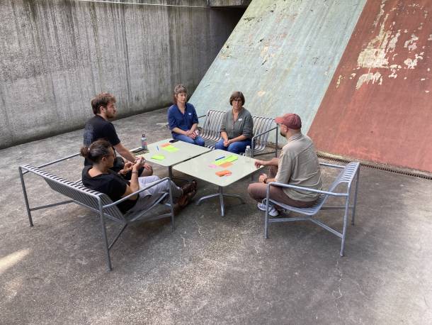 5 Personen sitzen draussen rund um einen Tisch und reden. Auf dem Tisch befinden sich Post-its.